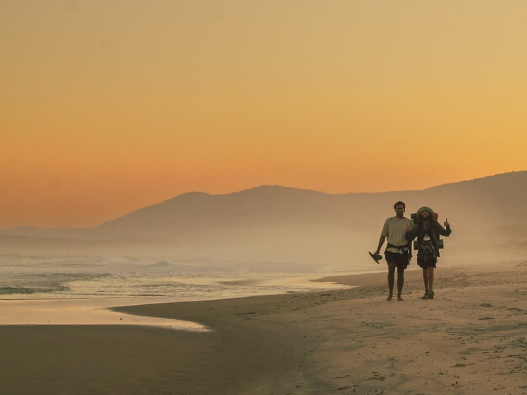 Dos mochileros caminando a la distancia por una playa en Tasmania, Australia